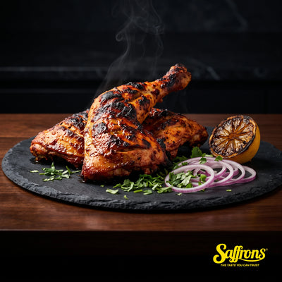 Charred tandoori chicken leg quarters on a dark slate platter with a charred lemon half, red onion rings and coriander